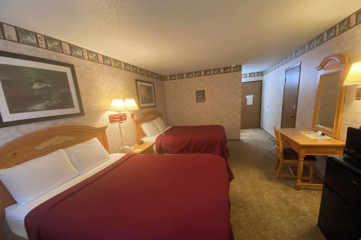 Habitación de hotel con dos camas, un escritorio, una silla, un aparador y un espejo.