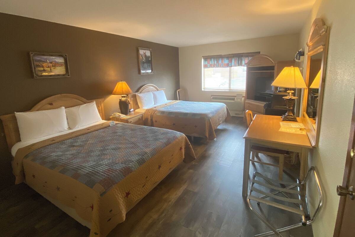 Habitación de hotel con dos camas, un escritorio, una silla, un espejo y una ventana con cortinas.