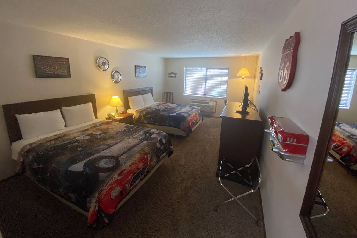 Habitación de hotel con dos camas, un escritorio, una silla, una lámpara, un calefactor y una ventana con persianas.