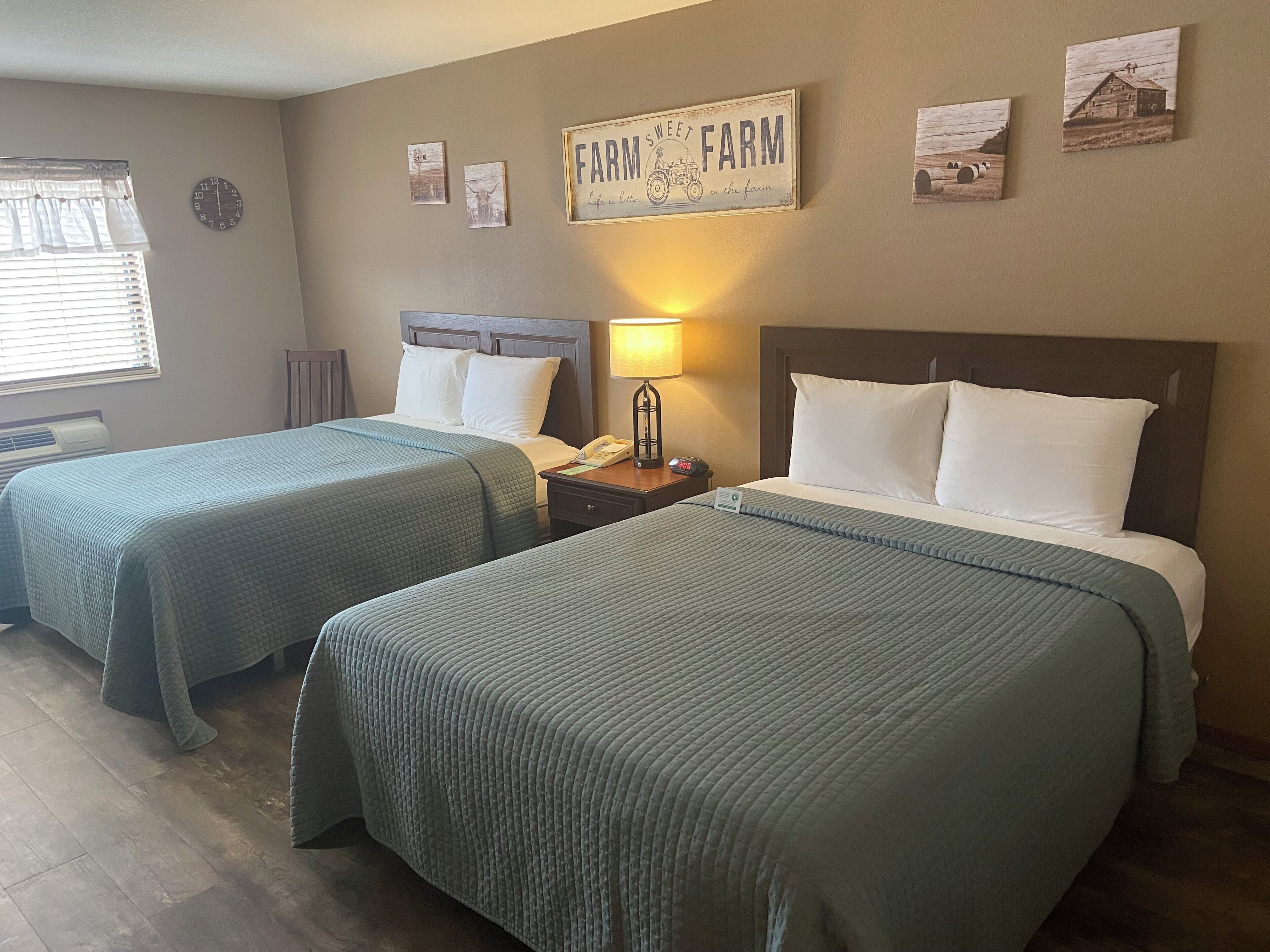 Habitación de hotel con dos camas, un reloj y decoración en la pared, incluyendo un letrero que dice 'Farm Sweet Farm'.