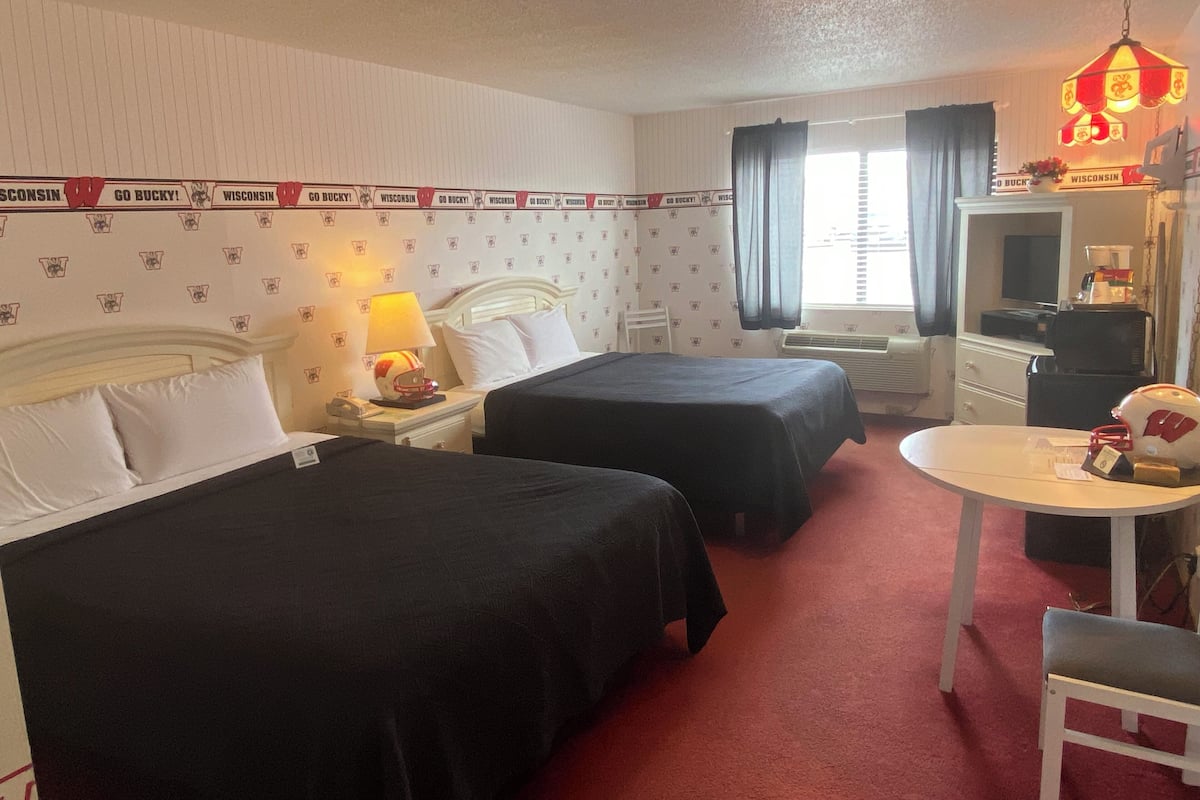 Una habitación de hotel con dos camas, un escritorio, una silla, una lámpara y un televisor.
