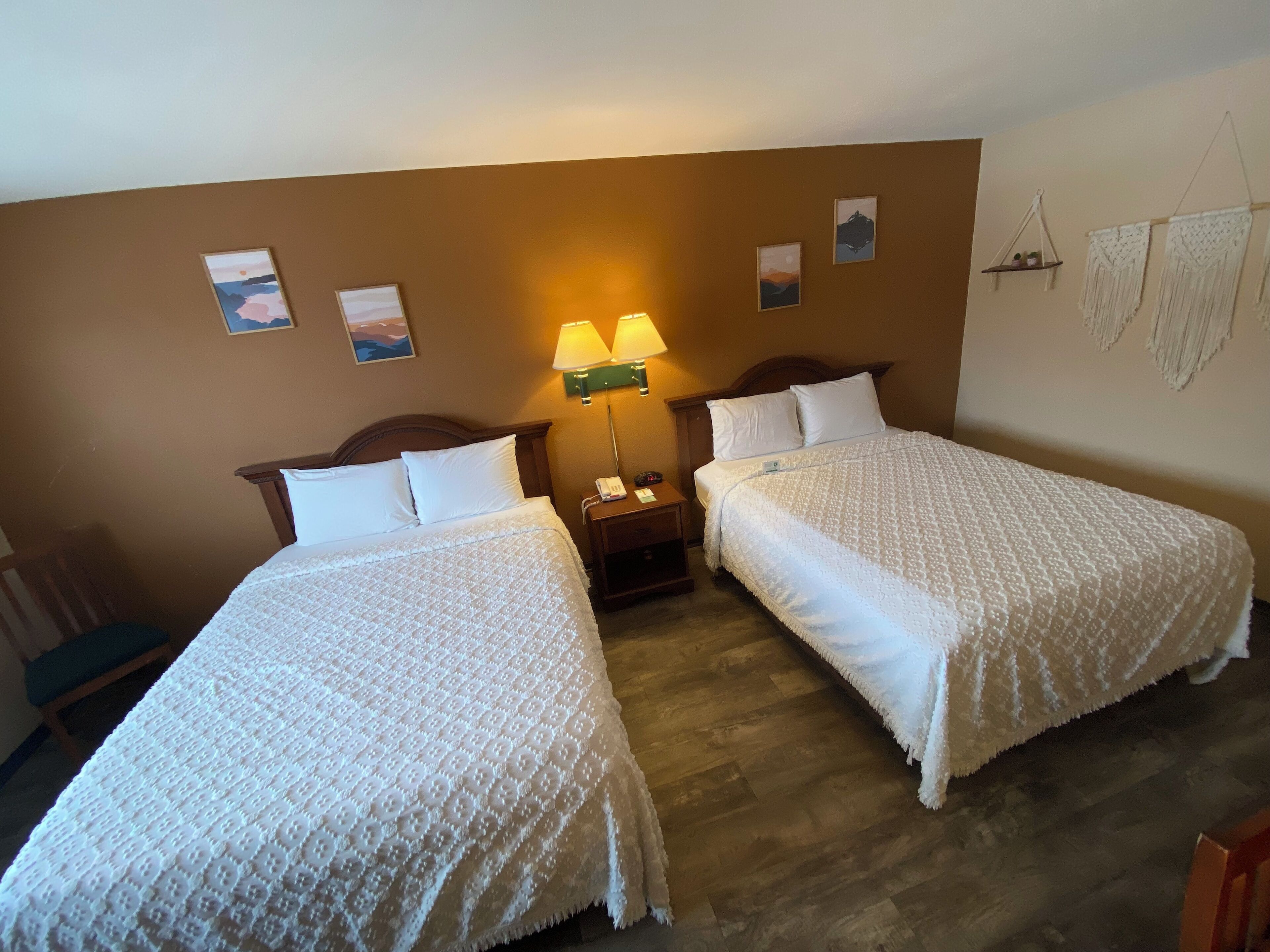 Camera d'albergo con due letti, un comodino con una lampada e opere d'arte alle pareti.