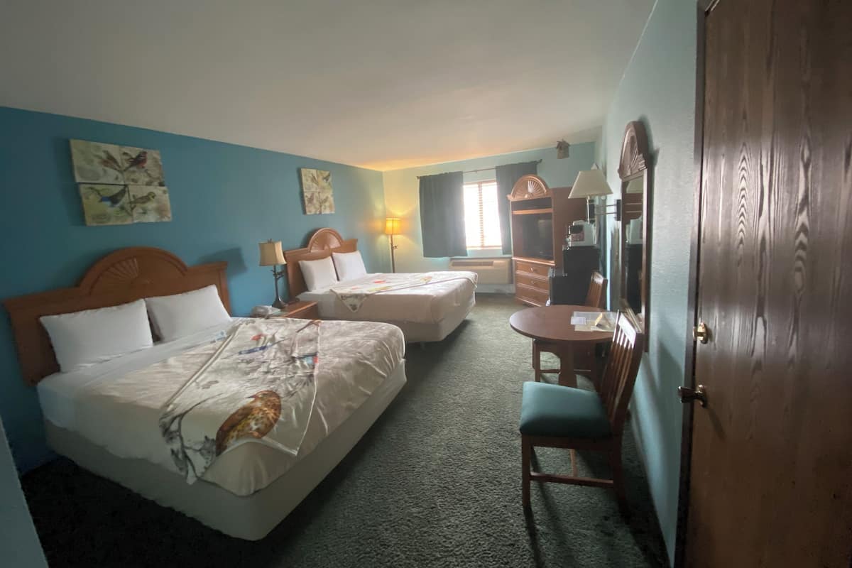 Habitación de hotel con dos camas, un escritorio, una silla, un aparador y un espejo.