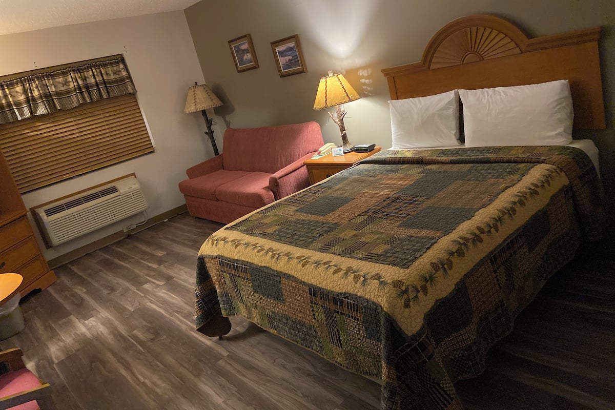 Un dormitorio con cama, una silla, una mesita de noche, una lámpara y un calentador instalado en la pared.