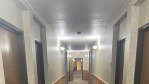 A long, carpeted hallway with wooden paneling on the walls and doors, leading to an exit sign at the end. - Pioneer Motor inn (Westfield)