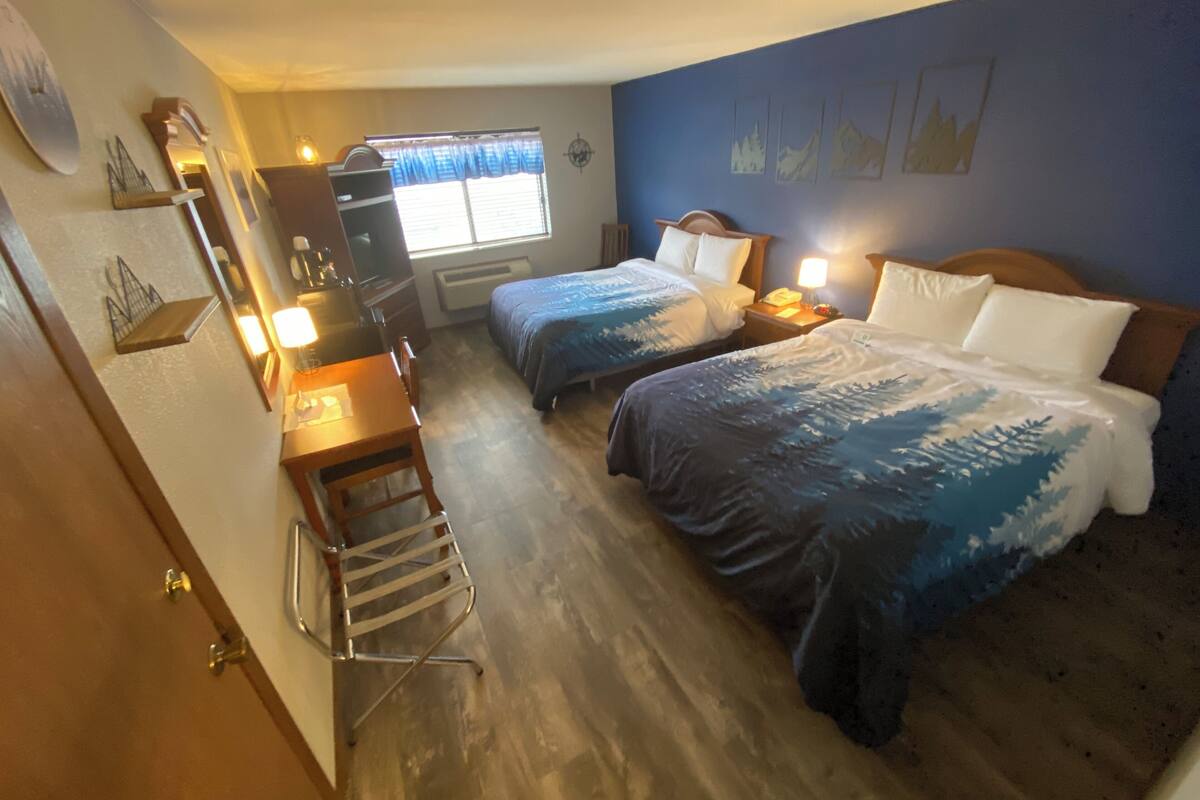 Habitación de hotel con dos camas, un escritorio, una silla, una lámpara y una ventana con cortinas.
