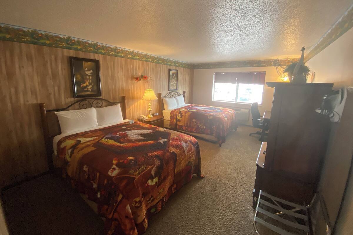 Habitación de hotel con dos camas, un escritorio, una silla, una lámpara y una ventana con cortinas.