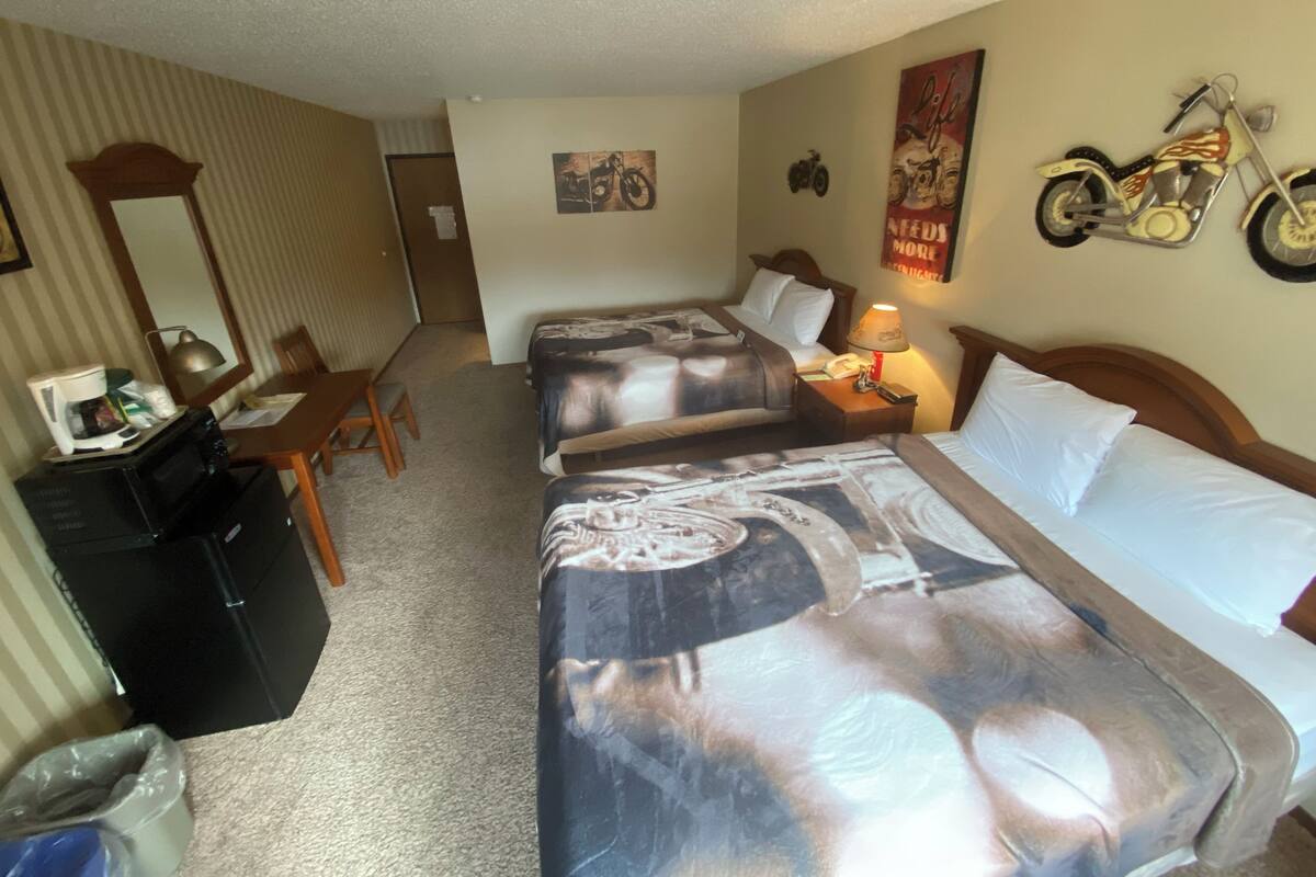 Una habitación de hotel con dos camas, un escritorio con cafetera, una silla y un cubo de basura.