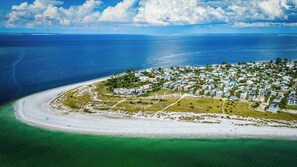 An aerial view of a coastal resort with beachfront properties, clear skies, and a calm sea.