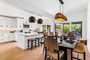 A modern kitchen with white cabinets, a central island, and a dining area with a large table and chairs. - Heated Pool | Spa | Free Golf Cart | Steps 2 Beach (Anna Maria)