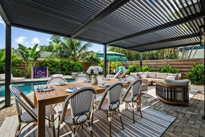 An outdoor patio with a pool, dining table, chairs, and a sofa.