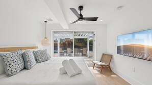 Quarto de hotel moderno com uma cama grande, ventilador de teto e vista para o exterior através de portas de vidro.