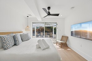 A modern hotel room with a large bed, ceiling fan, and a view of the outdoors through glass doors. - Rod and Reel Retreat | Heated Pool & Spa | Steps to Beach | Golf Cart (Anna Maria)