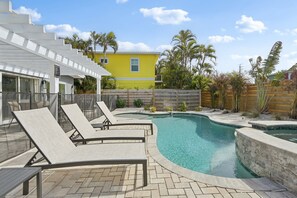 A pool area with lounge chairs, a yellow building, and palm trees. - Rod and Reel Retreat | Heated Pool & Spa | Steps to Beach | Golf Cart (Anna Maria)