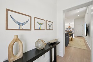 A hallway with framed whale tail art, a wooden sculpture, and a textured vase on a console table. - Rod and Reel Retreat | Heated Pool & Spa | Steps to Beach | Golf Cart (Anna Maria)
