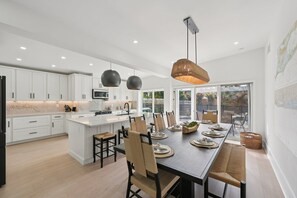 Une cuisine moderne avec des meubles blancs, un îlot central et un coin repas comprenant une longue table et des chaises.