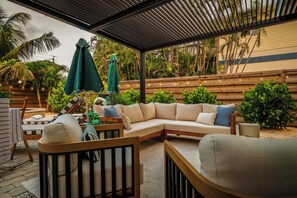 A covered outdoor seating area with a sofa, chairs, and umbrellas. - Heated Pool | Spa | Free Golf Cart | Steps 2 Beach (Anna Maria)