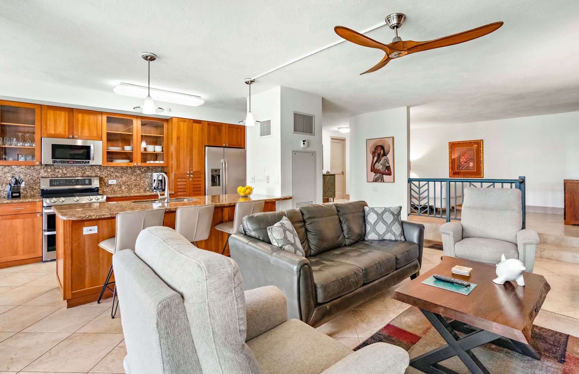 A modern living room with a grey sofa, a coffee table, and a TV. There is a kitchen area with wooden cabinets and a microwave.