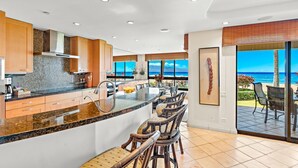 Une cuisine moderne dotée d’un grand îlot central, de meubles en bois et offrant une vue sur l’océan.