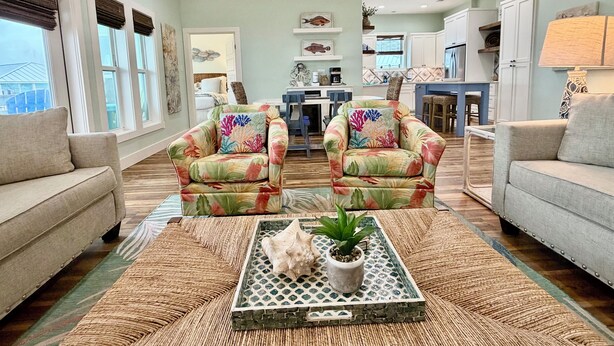 A spacious living room with two armchairs, a sofa, a coffee table with a plant, and a kitchen in the background. - Private Pool, Shared Pool, Boardwalk to the Beach (Port Aransas)