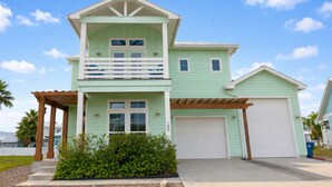 A two-story house with a garage, a balcony, and a well-maintained front yard. - Private Pool, Shared Pool, Boardwalk to the Beach (Port Aransas)