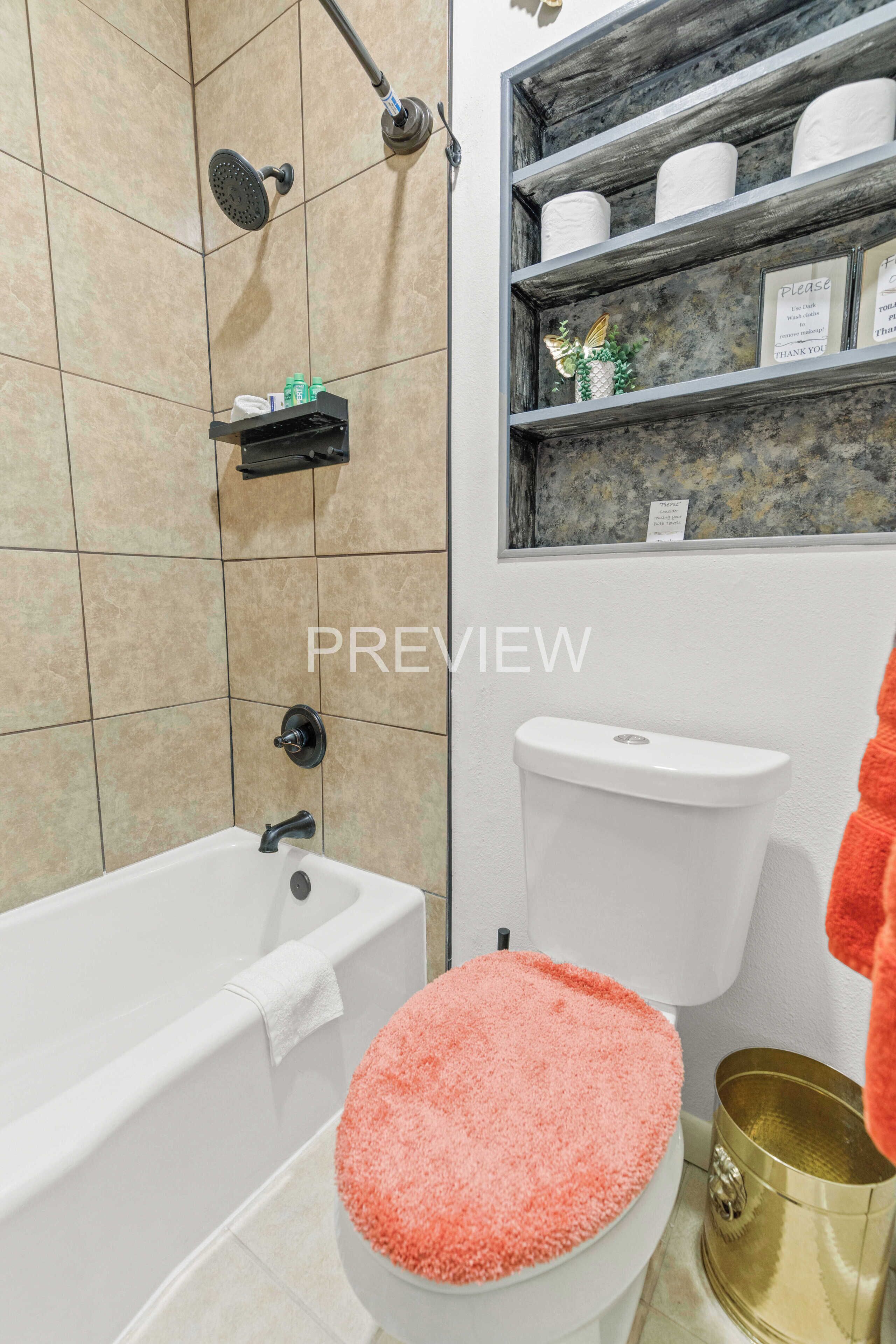 Une salle de bain équipée d’une baignoire, de toilettes et d’une douche. On y trouve des étagères avec des articles de toilette et un objet décoratif accroché au mur.