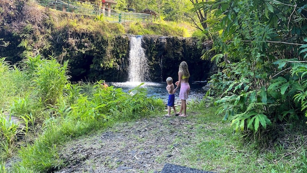 A natural setting with a waterfall, lush greenery, and a paved path. - World Famous  Big Wave Camper (Wailuku)