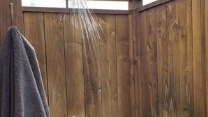 A wooden shower enclosure with a towel hanging on the door, a metal handle, and a wooden deck outside. - World Famous  Big Wave Camper (Wailuku)