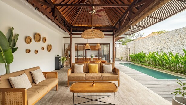 A modern outdoor living area with a wooden ceiling, a sofa, a coffee table, and a pool. - Villa Ivory 8Min Beach Pecatu byOrivista (Pecatu)