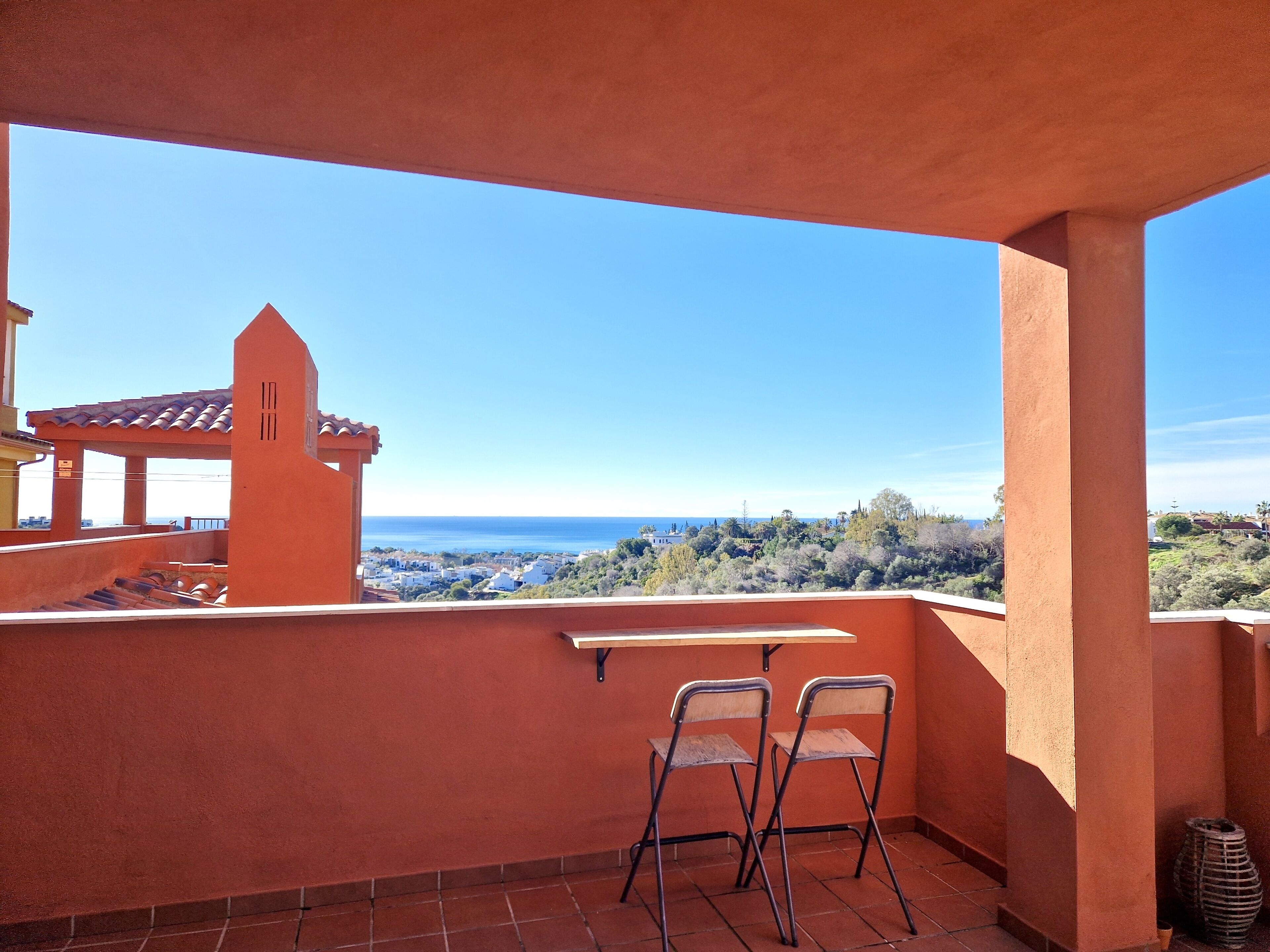 A balcony with two chairs, a small table, and a view of the sea and town.