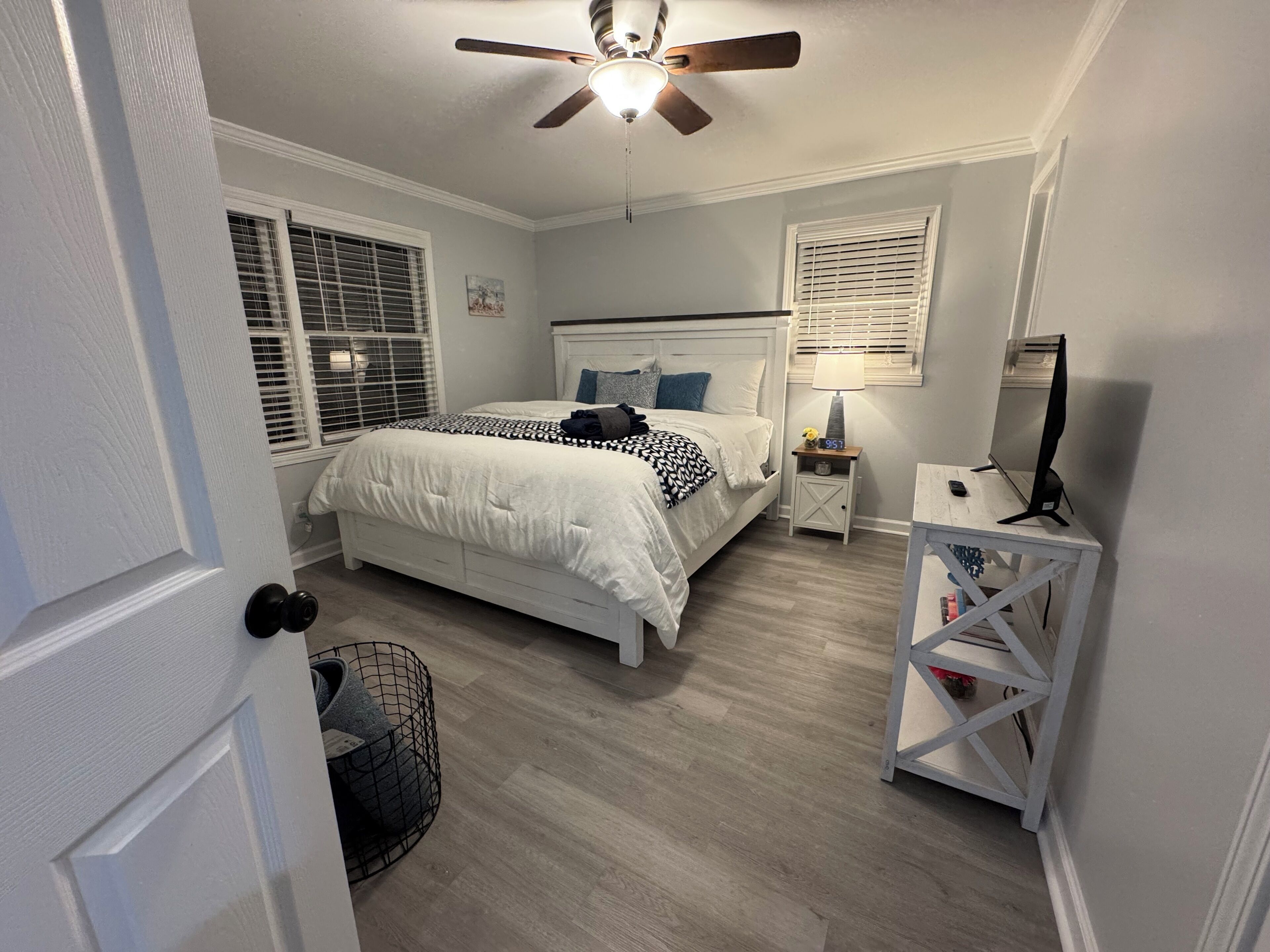Un dormitorio con cama, mesita de noche, escritorio, ventilador de techo y ventana con persianas.