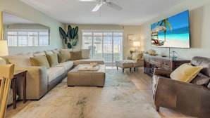 A living room with a beige sofa, a brown leather couch, a coffee table, and a TV displaying a beach scene.