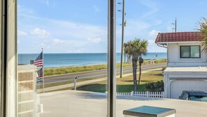 A view from inside a building looking out to the beach, with an American flag and a white fence visible.