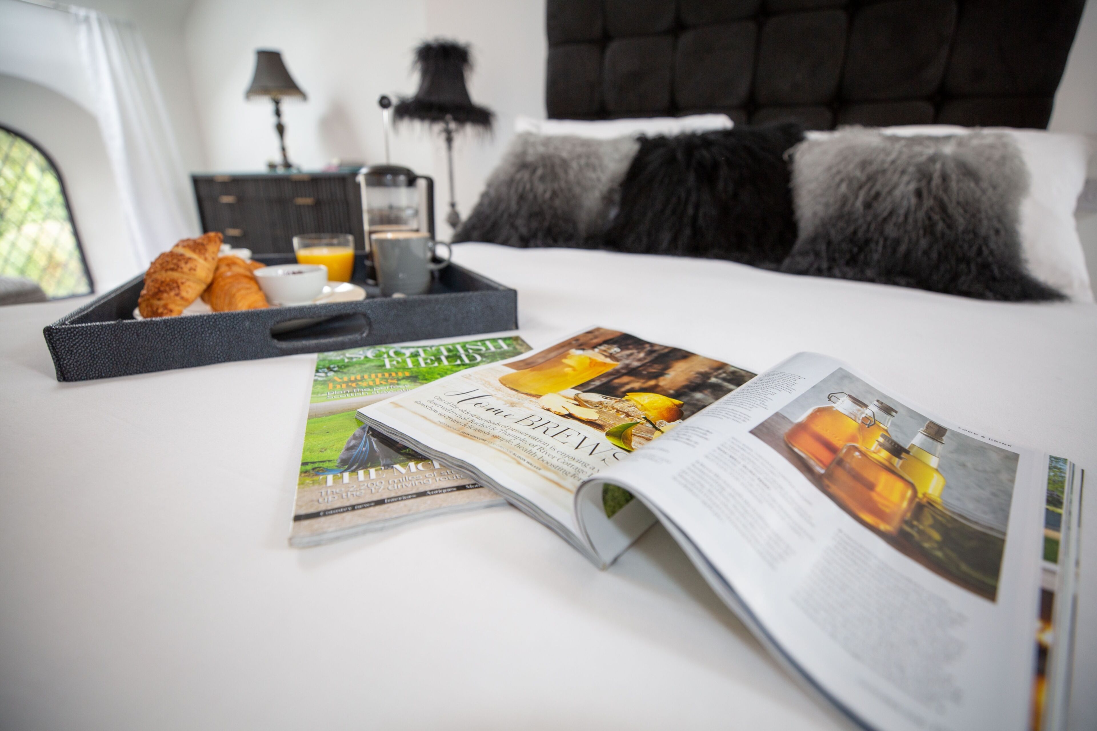 A neatly made bed with a magazine, a tray with croissants, and a glass of orange juice.