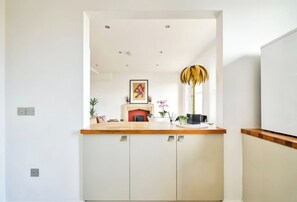 Eine moderne Küche mit weißen Schränken, einer Holz Arbeitsplatte, einem Kamin und einer Zierpflanze.