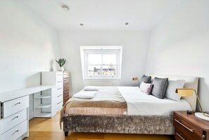 Een moderne slaapkamer met een groot bed, een dressoir, een nachtkastje en een raam met uitzicht over de stad.
