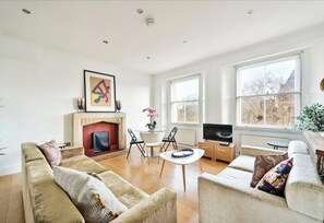 Ein geräumiges Wohnzimmer mit Kamin, bequemen Sitzgelegenheiten, einem Fernseher und großen Fenstern mit Blick ins Freie.