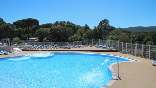 Una piscina con lettini e un'area recintata, immersa tra alberi e colline.