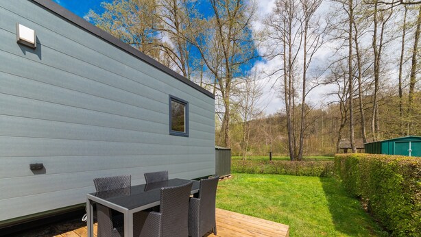 En moderne autocamper med terrasse, udendørs møbler og udsigt til frodig natur og træer.