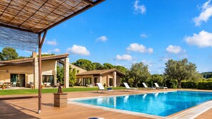 A poolside area with a wooden deck, lounge chairs, and a blue towel. - El Refugio Mediterráneo by Interhome (Begur)