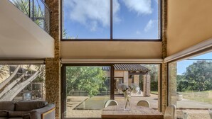 A spacious living area with a large wooden table, comfortable seating, and a view of a garden and outdoor seating area through large windows. - El Refugio Mediterráneo by Interhome (Begur)