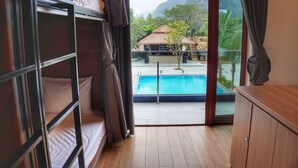 Ein Zimmer mit Etagenbetten, Holzboden, Blick auf ein Schwimmbecken und einem Bergpanorama.