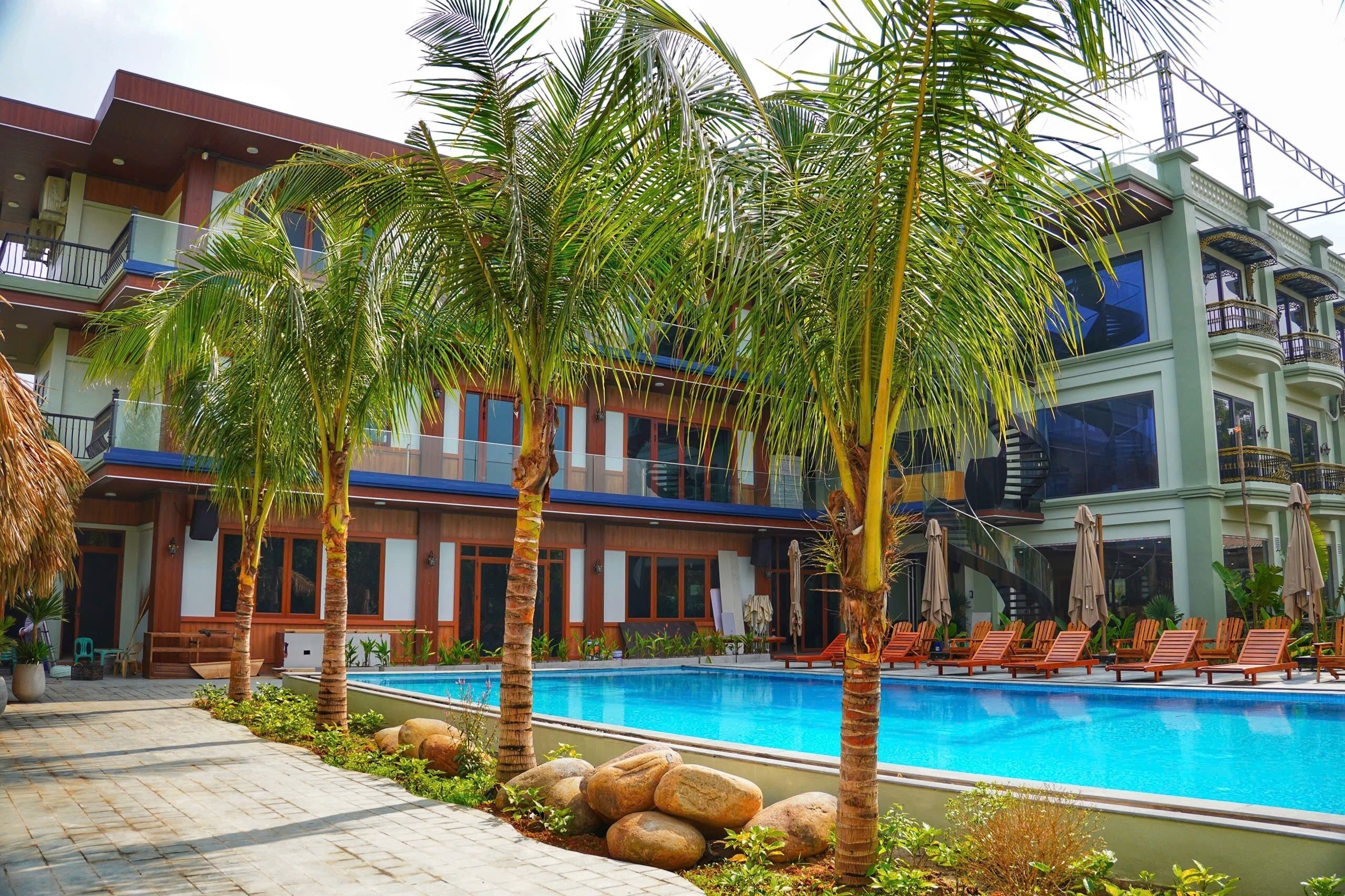 Un hotel con piscina, palmeras y un edificio moderno con balcones.