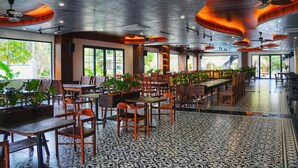 Ein geräumiges Restaurant mit Holztischen und -stühlen, großen Fenstern und Deckenventilatoren.
