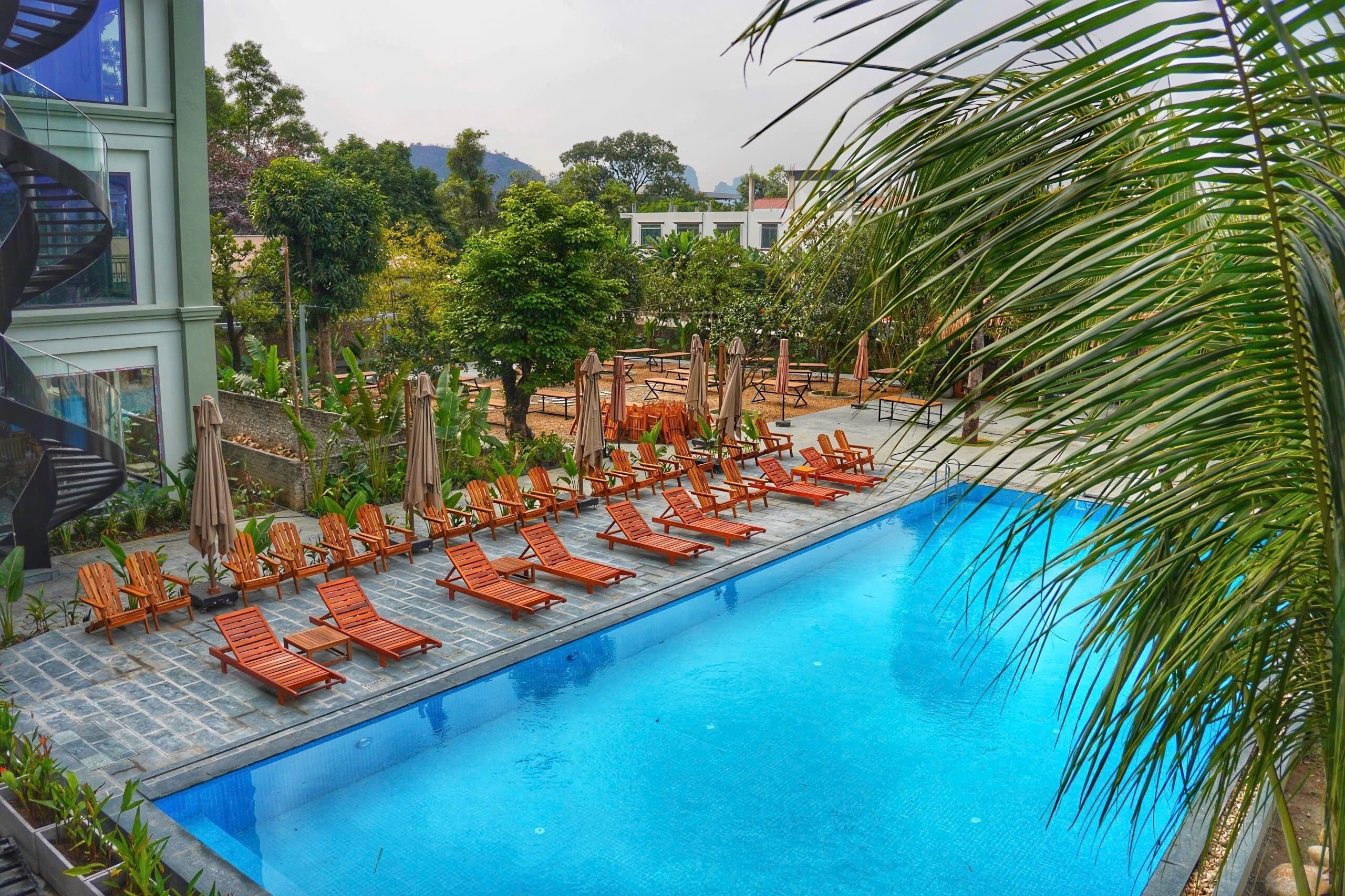 A pool area with sun loungers and umbrellas, surrounded by greenery and a modern building with a spiral staircase.