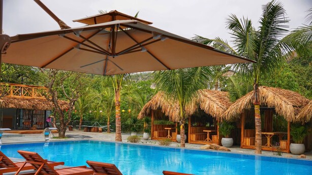 Ein Poolbereich mit Liegestühlen, strohgedeckten Pavillons und einem klaren, blauen Pool.