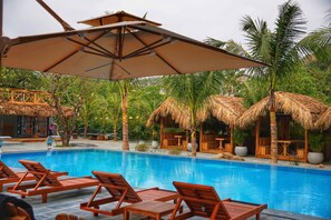A poolside area with lounge chairs, thatched-roof structures, and a clear blue pool. - The Luna Tam Coc Hostel - Bar & Pool (Nam Hoa Lu)