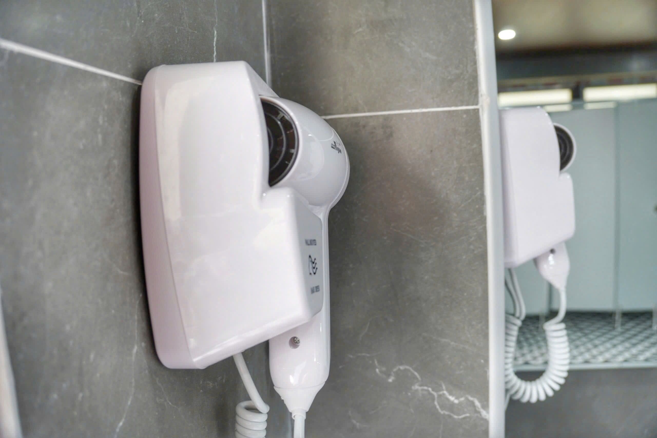 A wall-mounted hair dryer in a bathroom with a tiled floor.