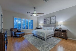 A bedroom with a bed, a chair, a dresser, a nightstand, and a ceiling fan.