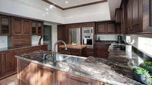 A modern kitchen with dark wood cabinets, granite countertops, stainless steel appliances, and a central island. - Princess Views-Pool & Spa-Walk to TPC Scottsdale (Scottsdale)